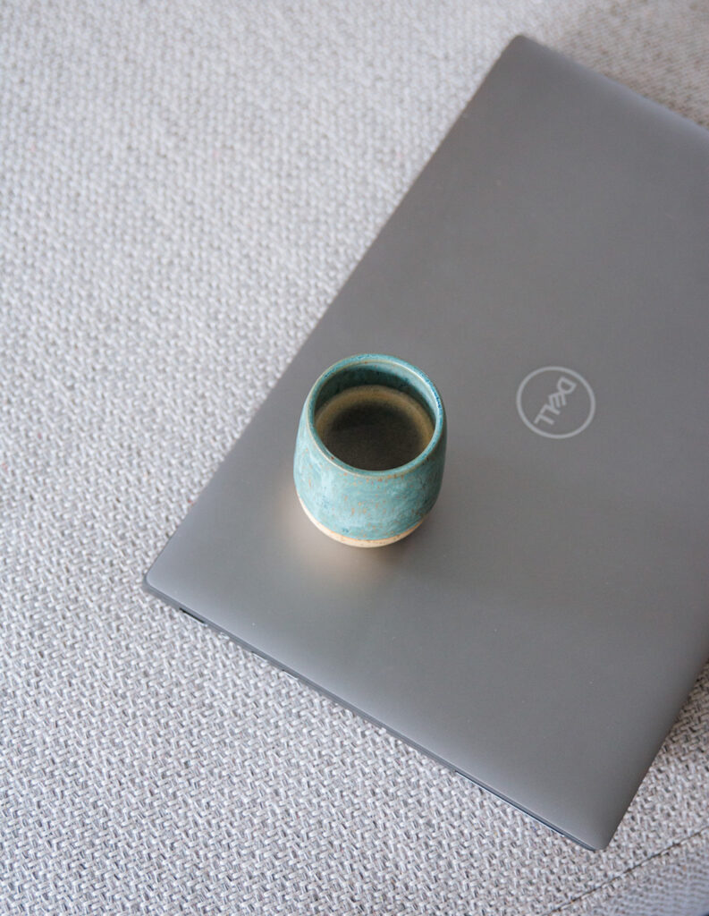 Gesloten laptop met een koffietas erbovenop, geplaatst op een stoffen zetel.